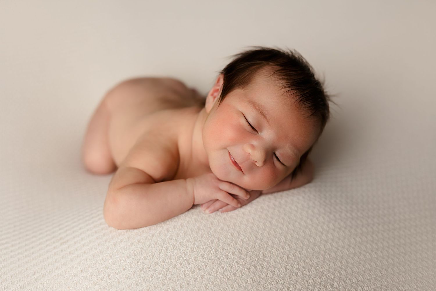 Sleeping newborn posed on textured cream blanket with simple minimalist backdrop.