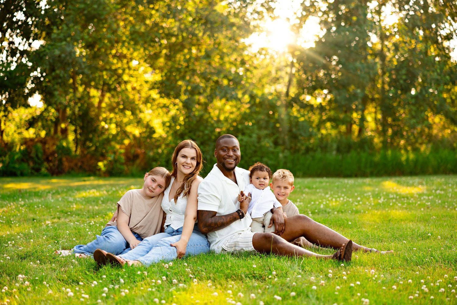 A multigenerational family relaxes together on lush grass during golden hour in a sunlit park.