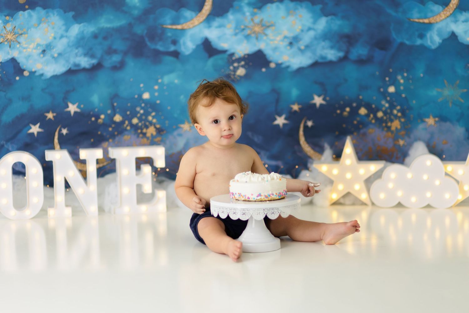 Celestial themed cake smash setup with stars, moons, and dreamy blue sky background.