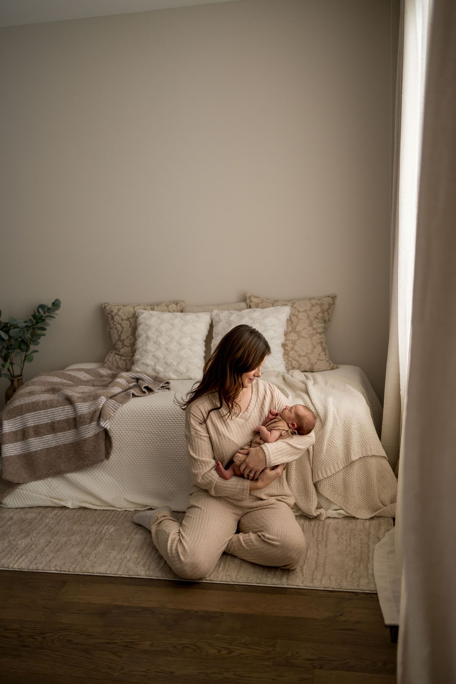 Person curled up on a beige couch in a minimalist room with white walls and wooden flooring.