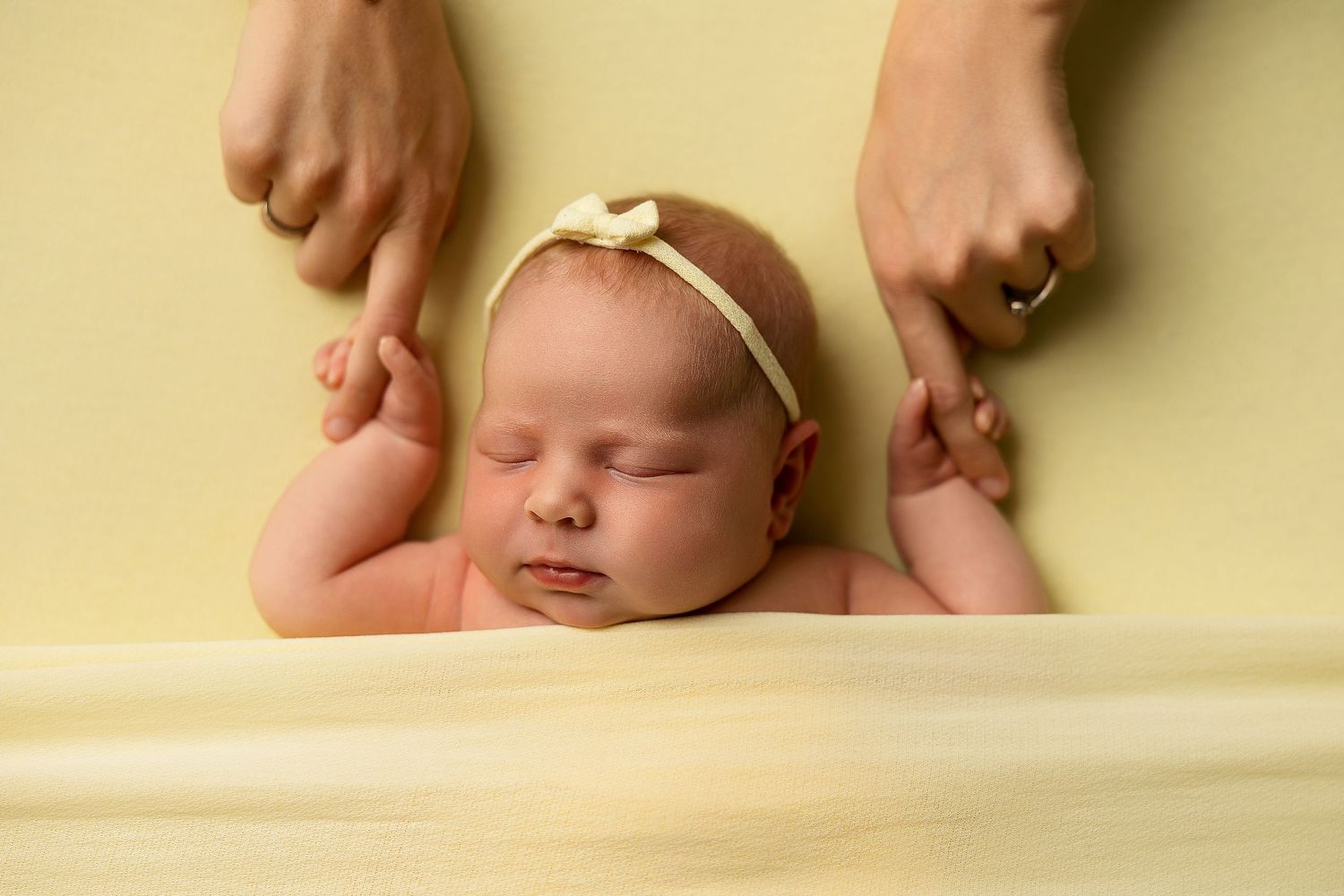 Sleeping baby on yellow backdrop with hands gently touching.