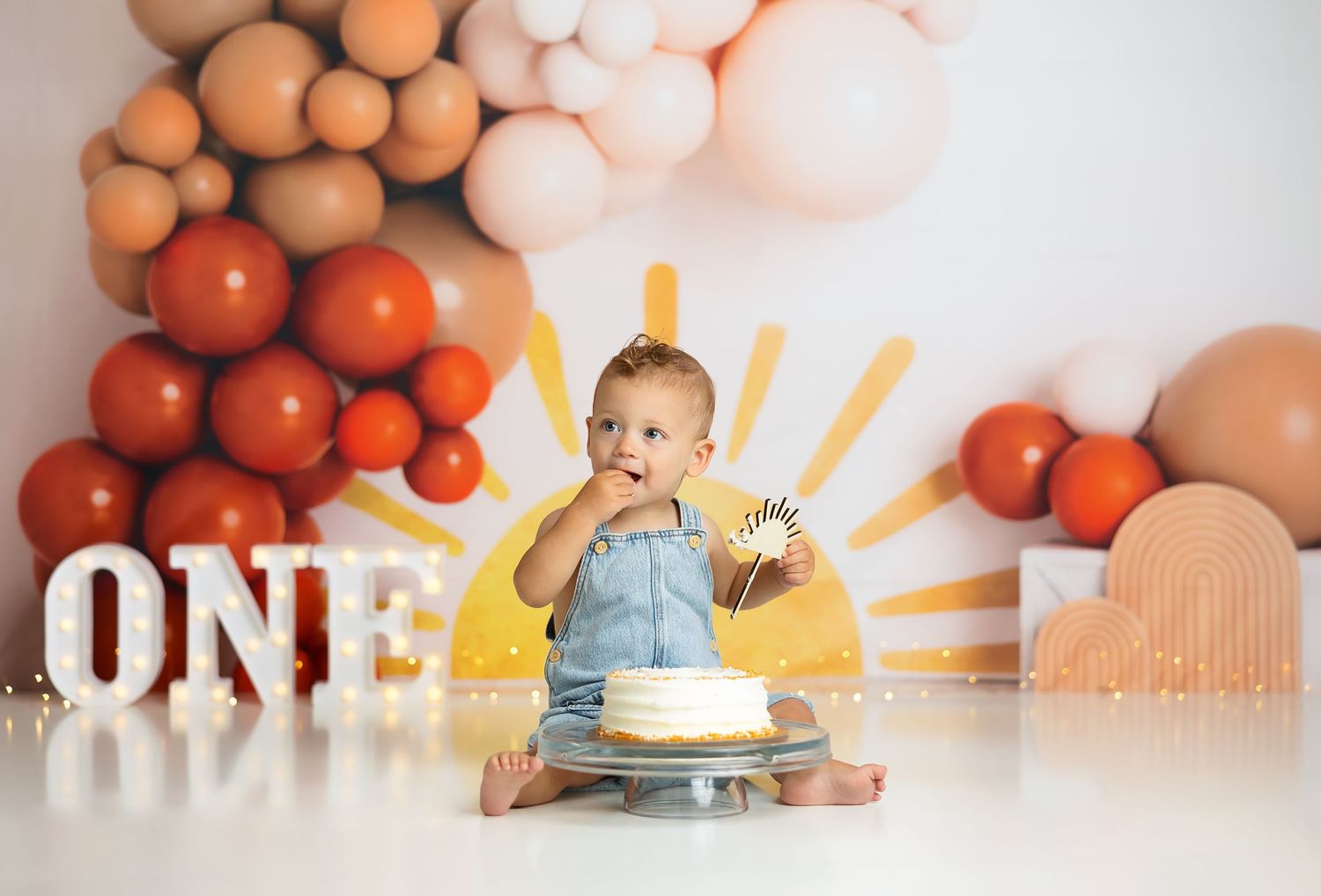 First birthday cake smash photo with decorative balloon arch and sunshine theme.