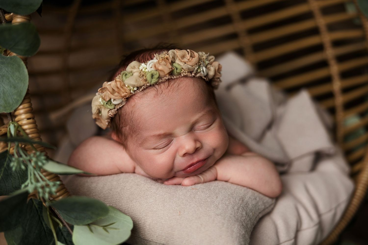 Sleeping baby with floral crown rests in basket with green foliage decor.