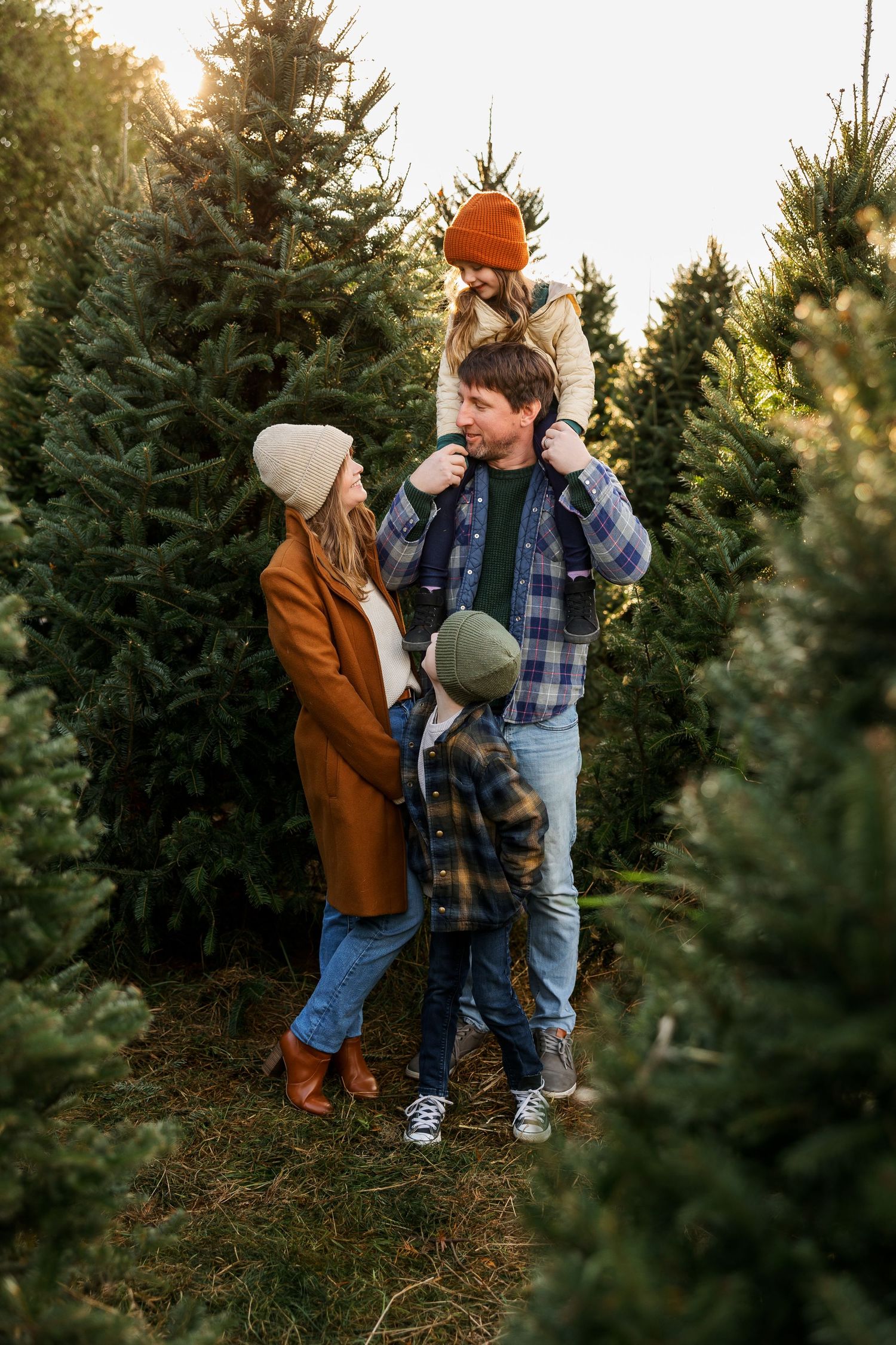 A playful scene at a Christmas tree farm with people holding colorful winter hats among evergreen trees.