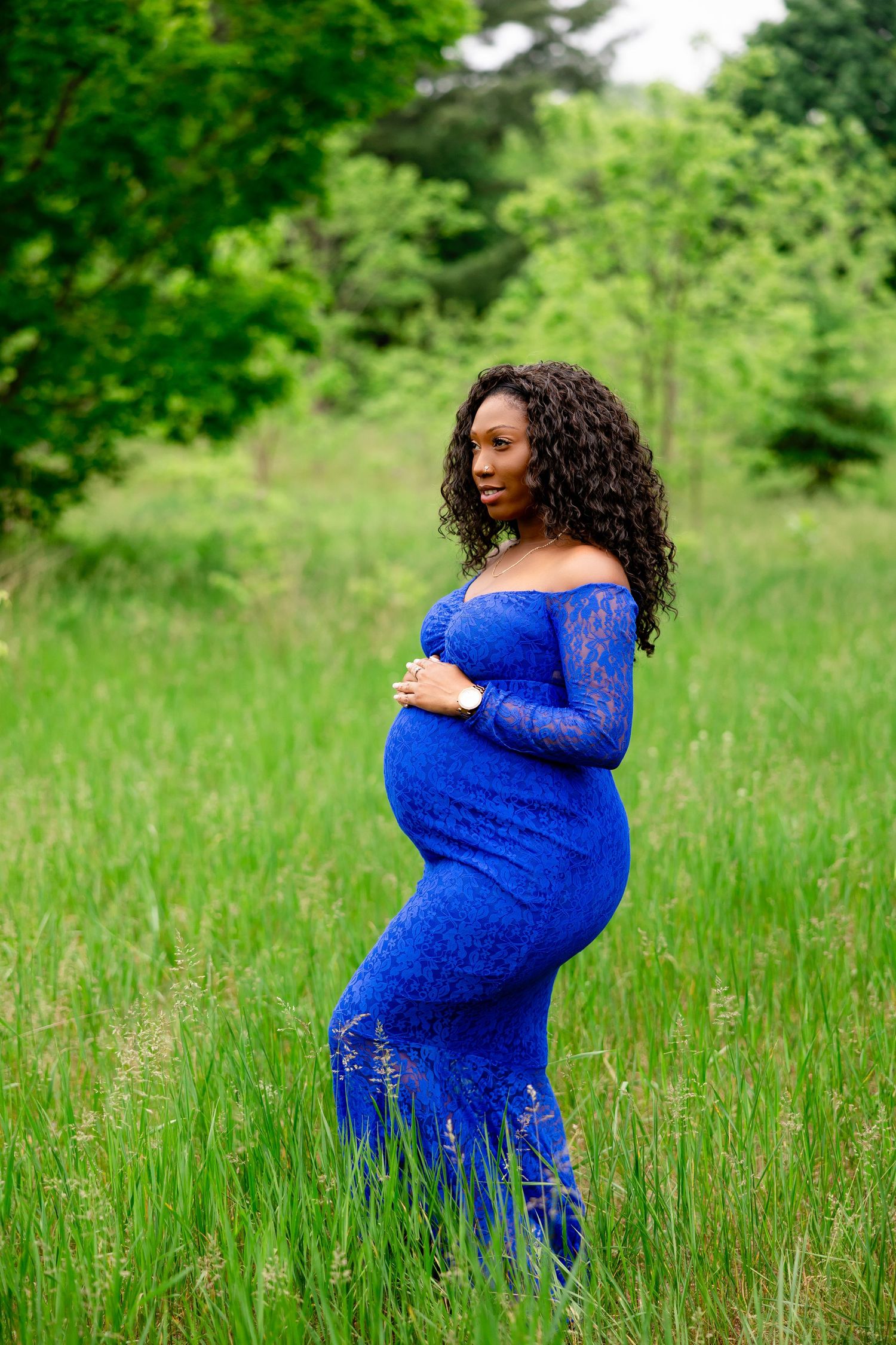 Maternity portraits of woman in blue lace dress posing in green summer field.