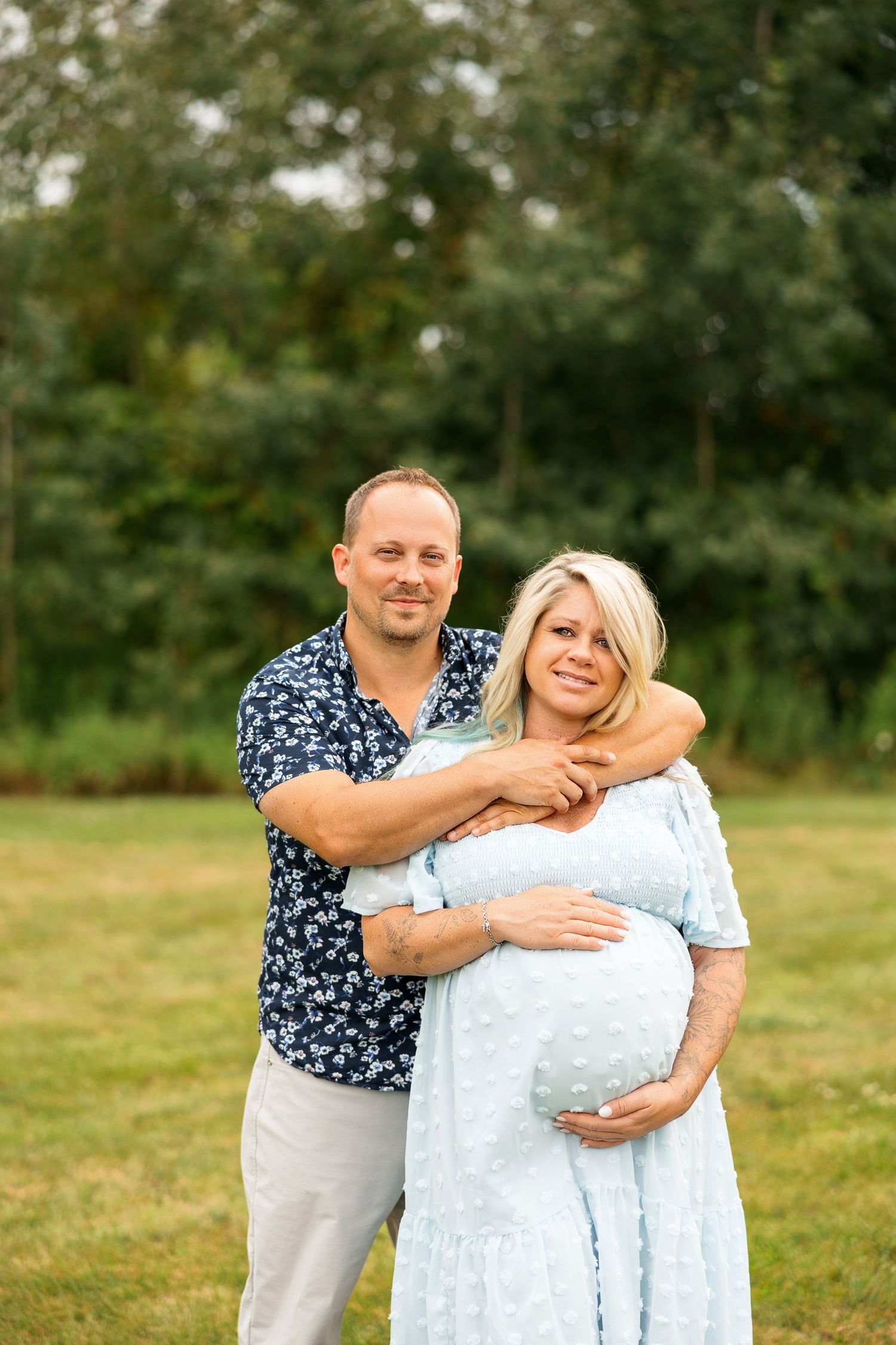 A playful couple shares a lighthearted moment while posing together in a grassy field on a sunny day.