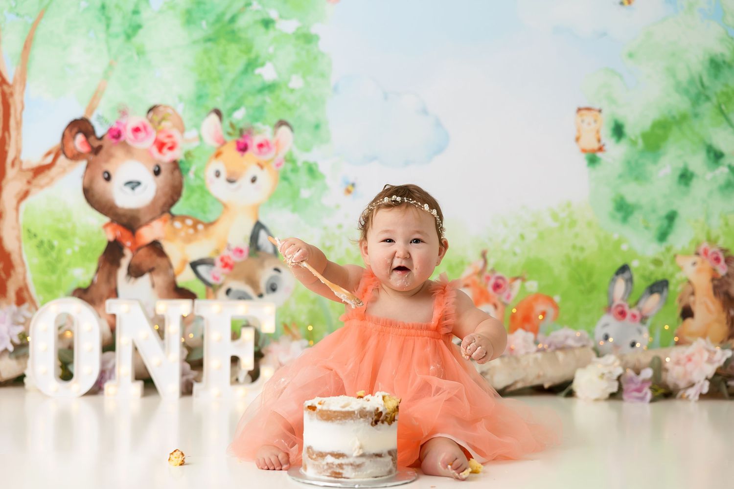 Woodland themed first birthday setup with floral backdrop and forest animals.