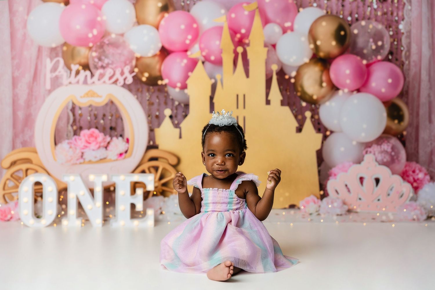 Pink and white balloon arch decorations with gold letters spelling 'ONE' for a first birthday party celebration.