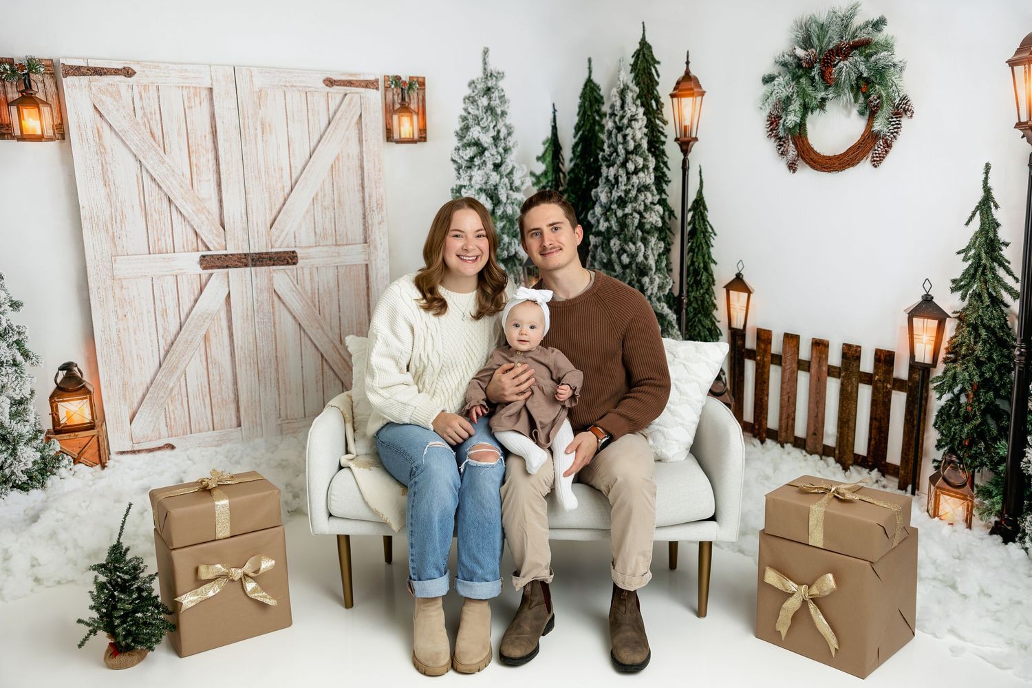 Family holiday portrait in front of rustic winter scene with wrapped presents and decorations.