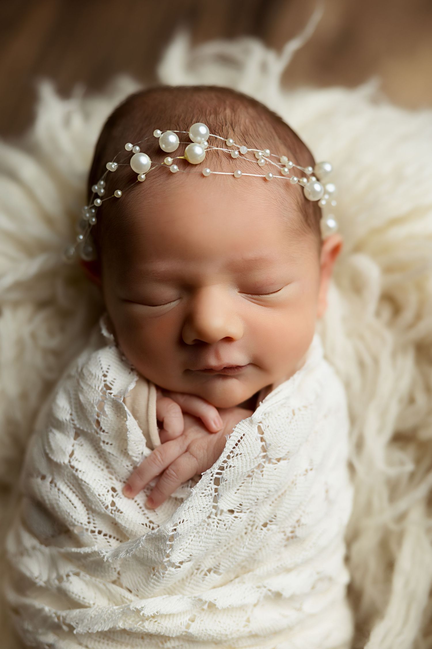 Sleeping newborn in white wrap with delicate pearl headpiece.