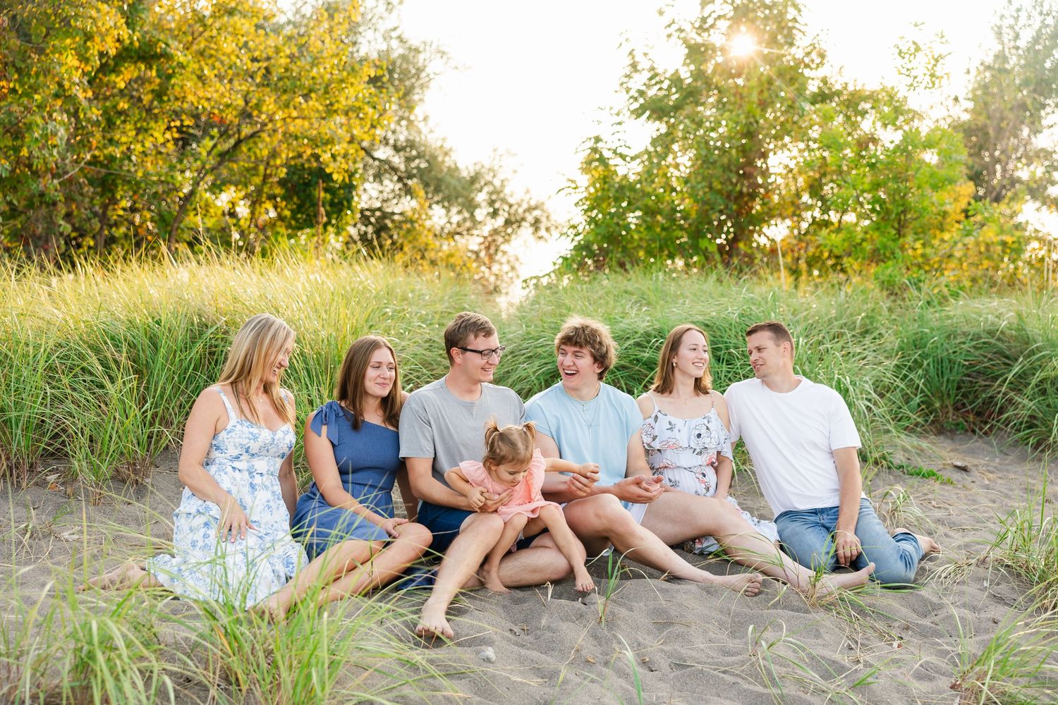 A group sits together on sandy ground with tall grass and yellow flowering trees in the background.