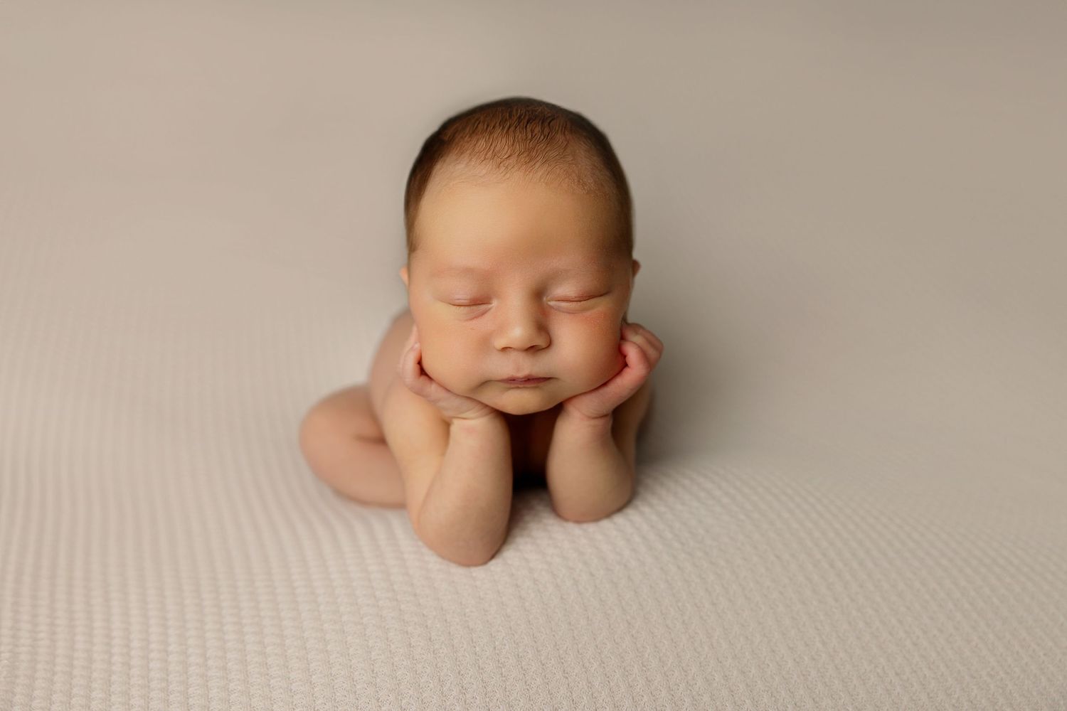 Sleeping newborn rests with hands under cheeks on textured grey backdrop.