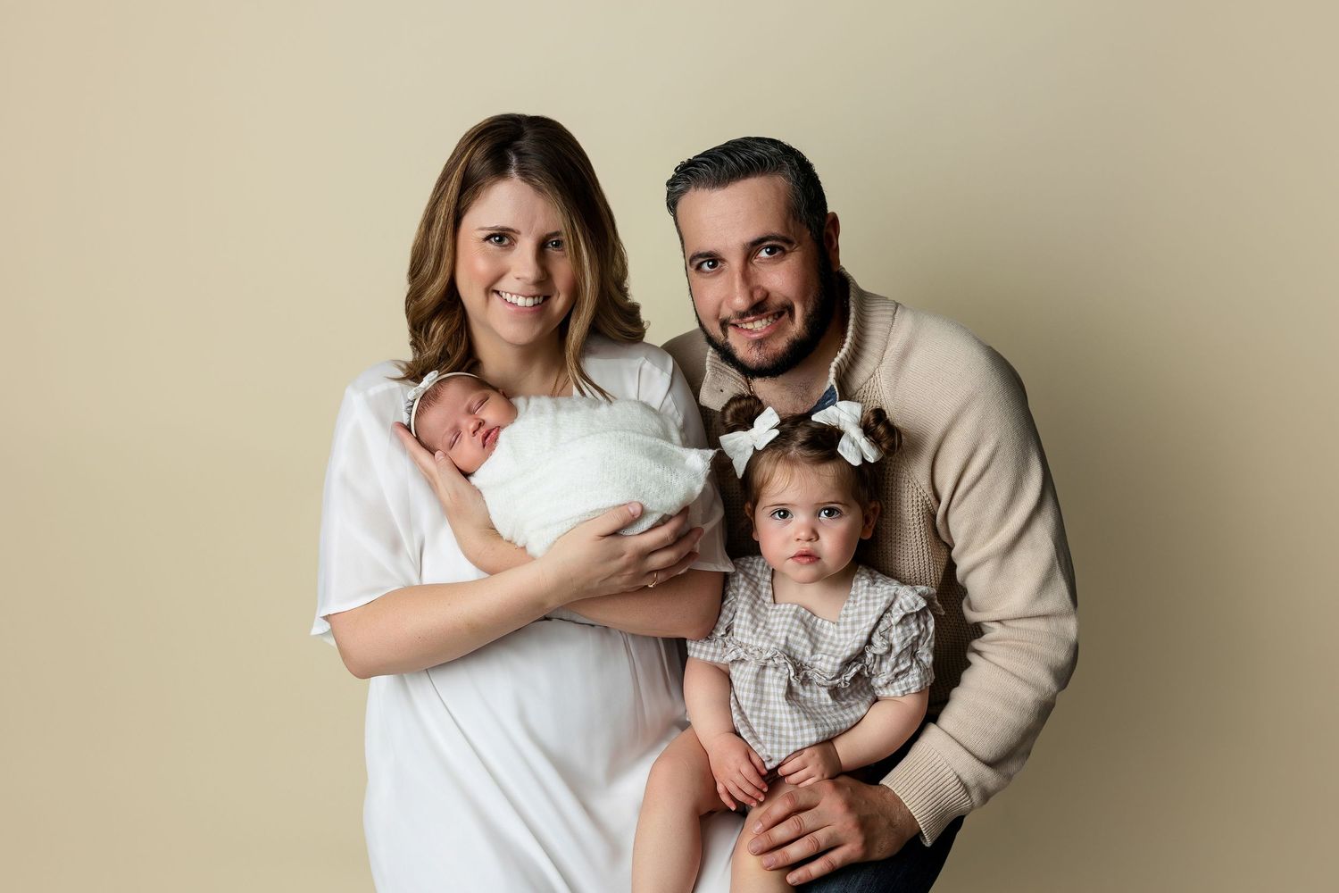Family portrait against beige backdrop in coordinated neutral outfits.