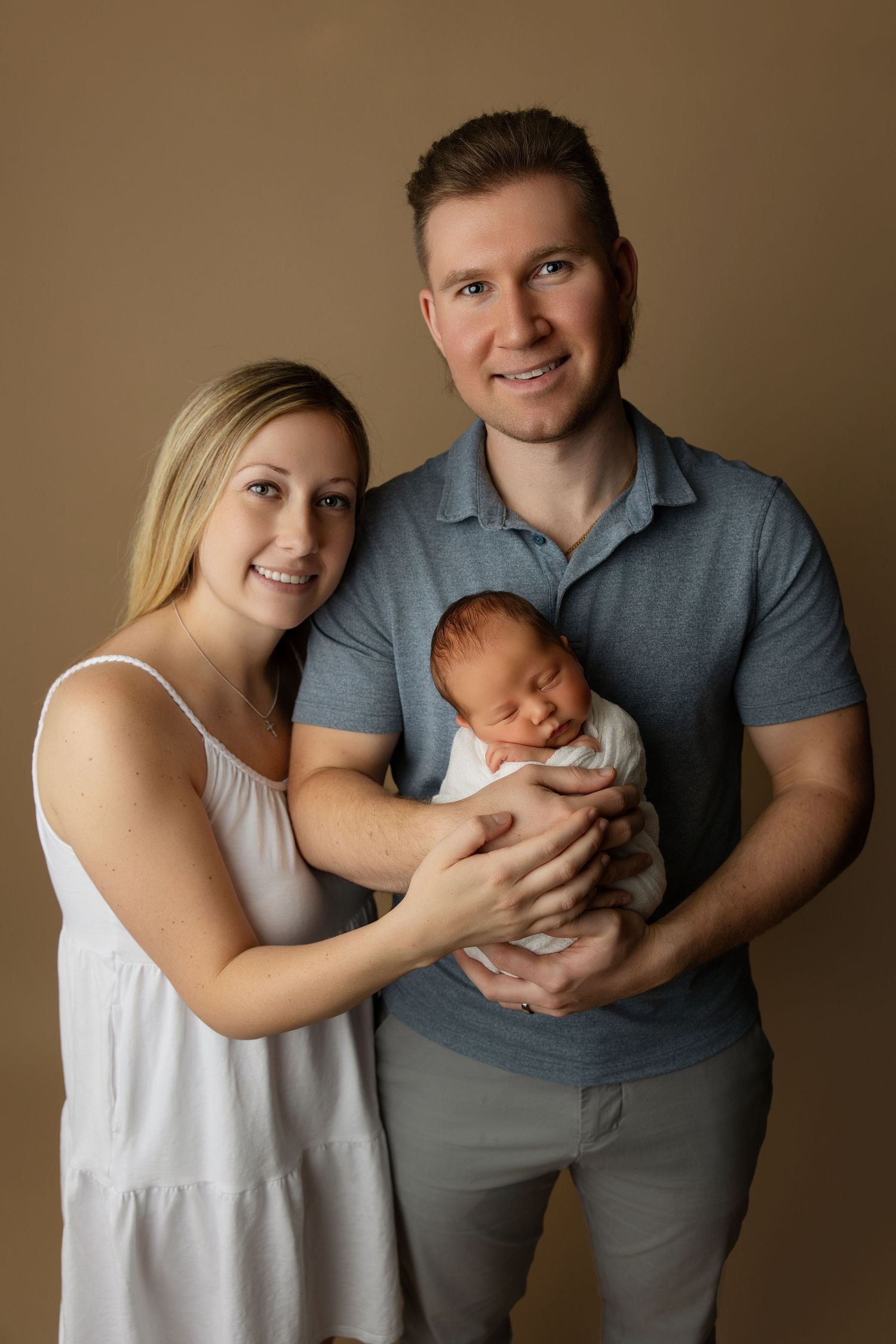 Studio portrait of new parents with baby against warm brown background.