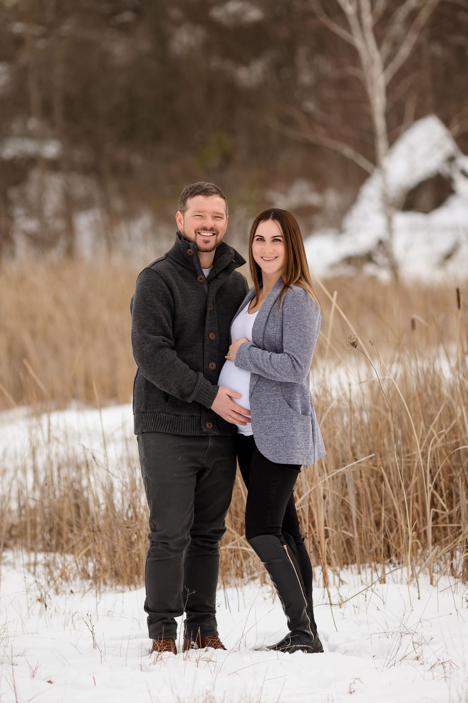 Winter maternity portrait in snowy field with brown rustic backdrop.