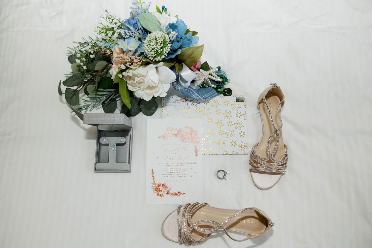Wedding details flatlay with blue floral bouquet, calendar and beige strappy sandals.