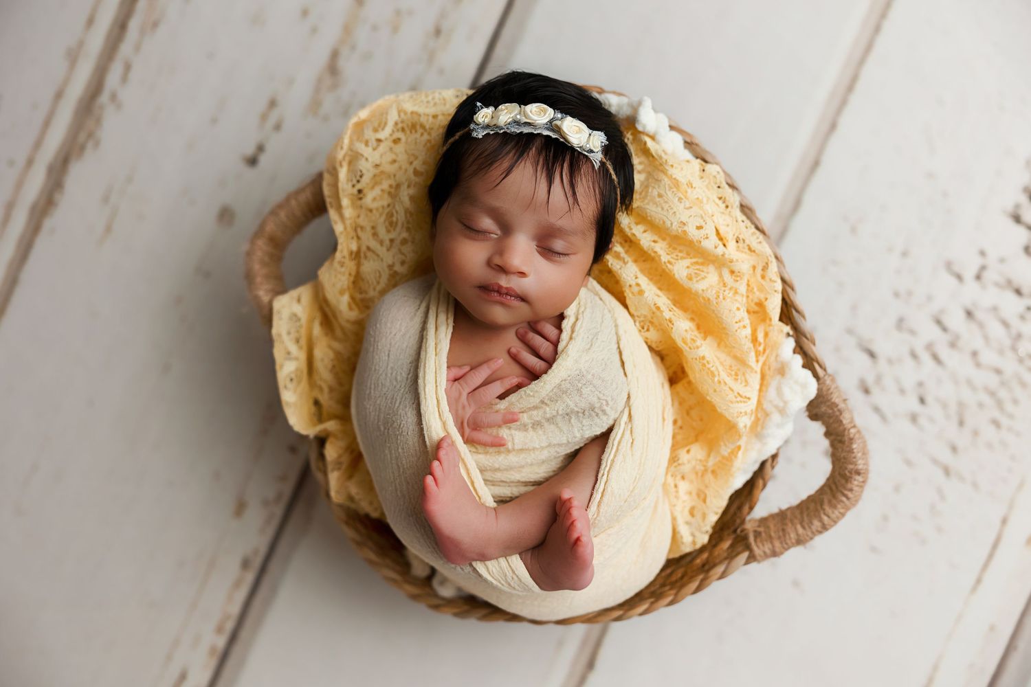 Peaceful newborn sleeping in woven basket with yellow and cream wraps.