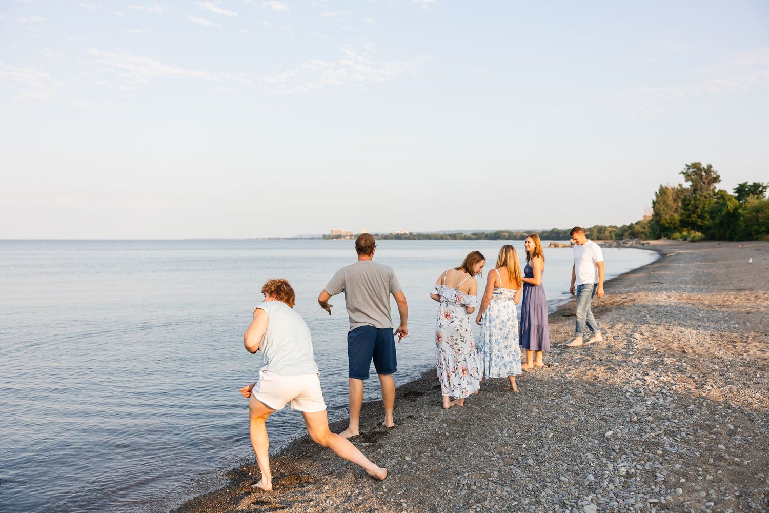 Group walks in a line along a peaceful beach shoreline during golden hour as calm waters stretch to the horizon.