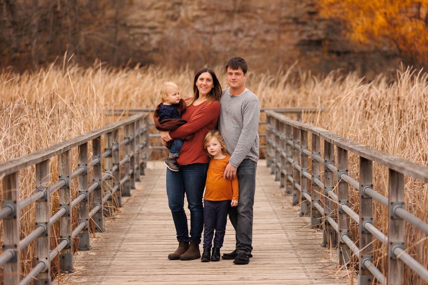 A family poses together on a wooden boardwalk surrounded by autumn marsh grass.