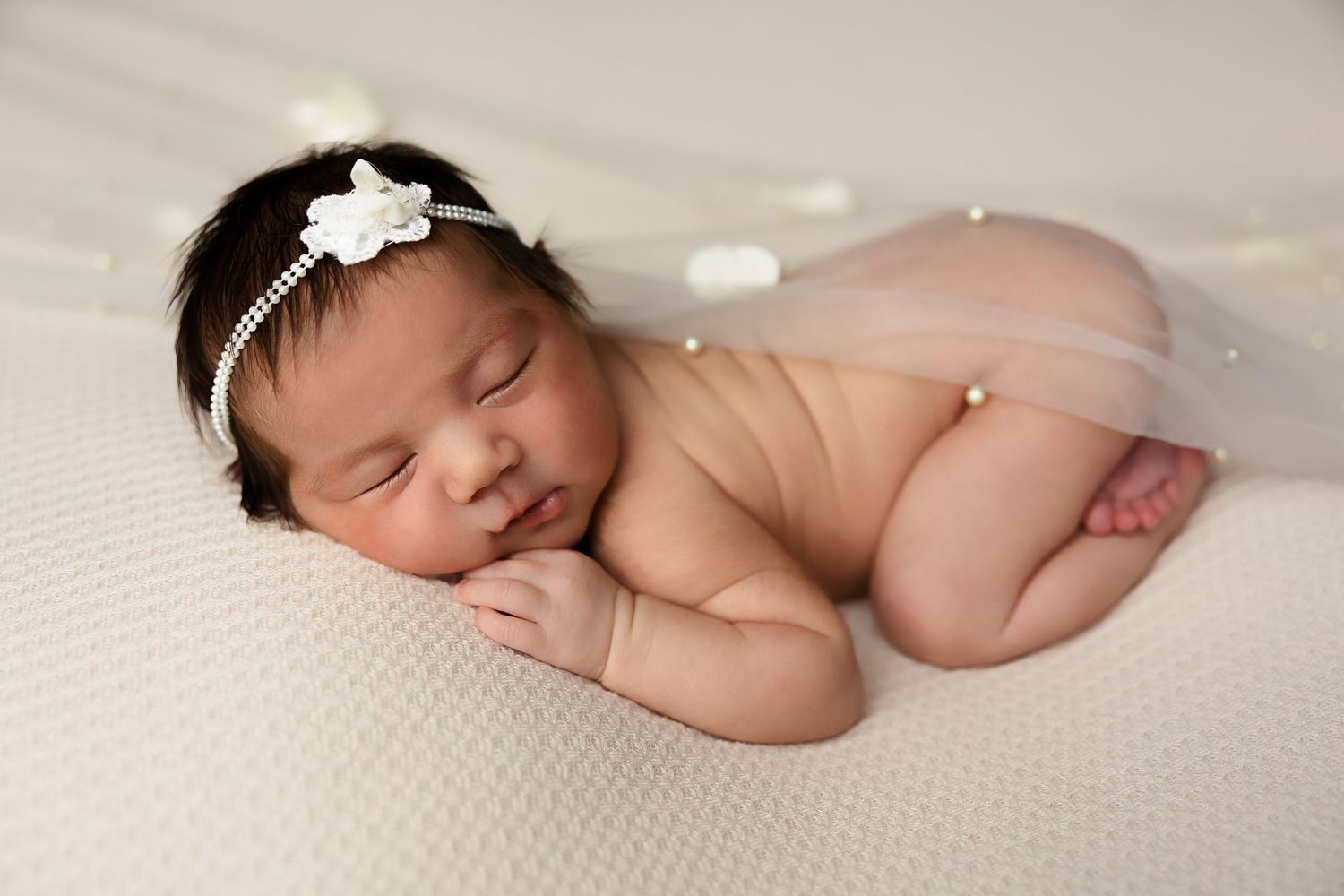 Sleeping newborn on white textured backdrop wearing delicate floral headpiece.