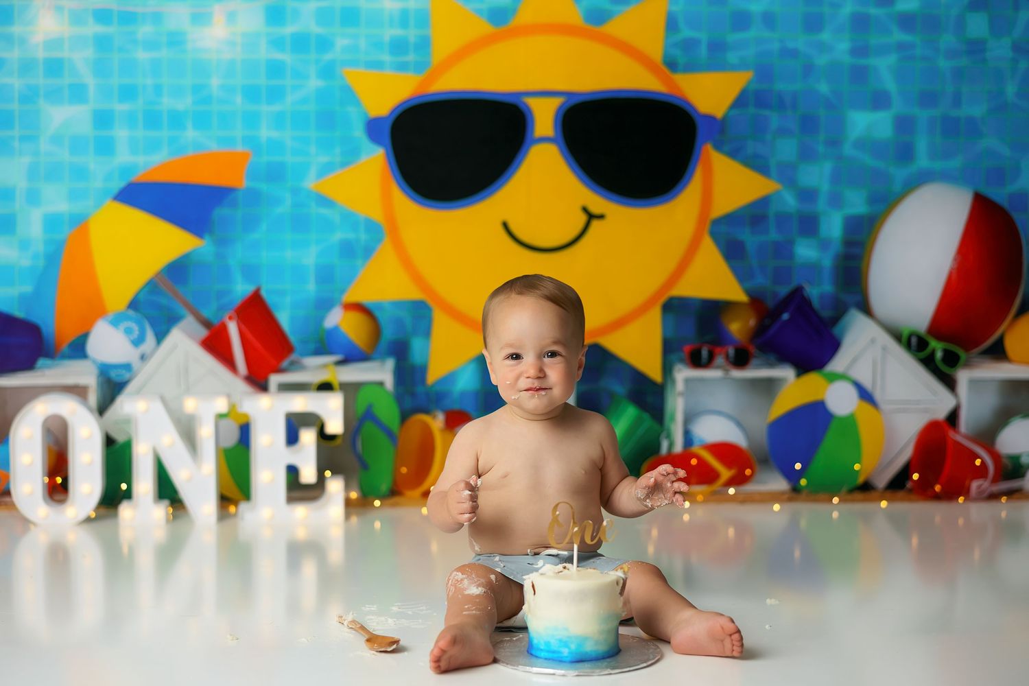 Baby's first birthday cake smash with colorful beach ball backdrop, sun decoration, and ONE sign.