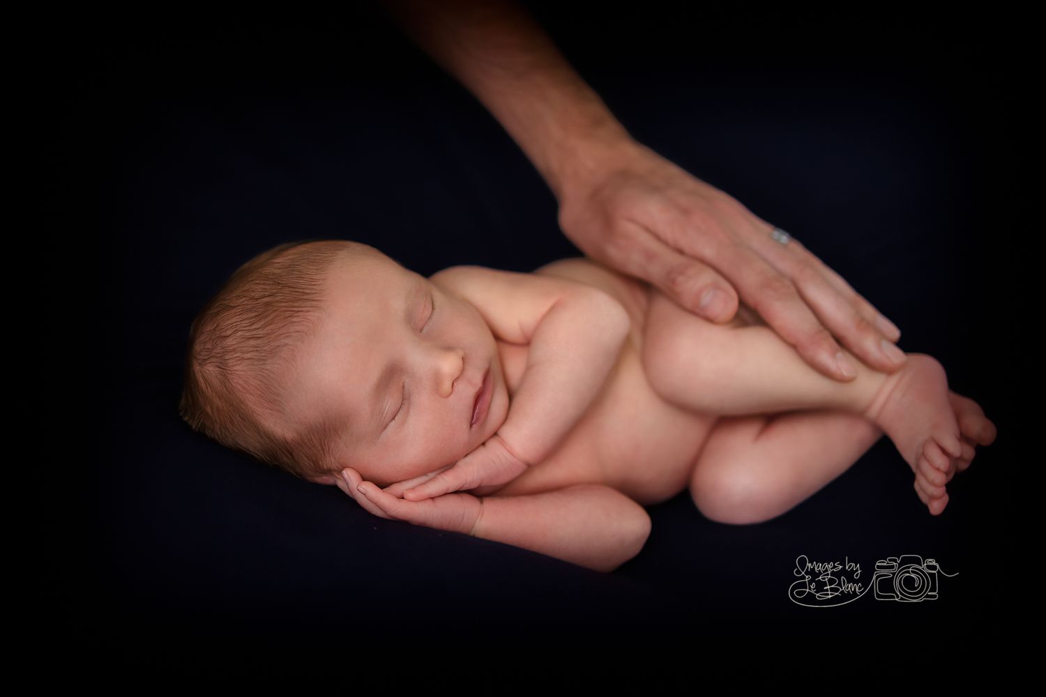 Newborn baby sleeping peacefully while being gently cradled on dark backdrop.