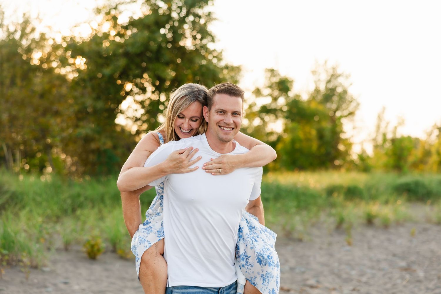 Playful couple enjoying a piggyback ride outdoors during golden hour with trees in background.