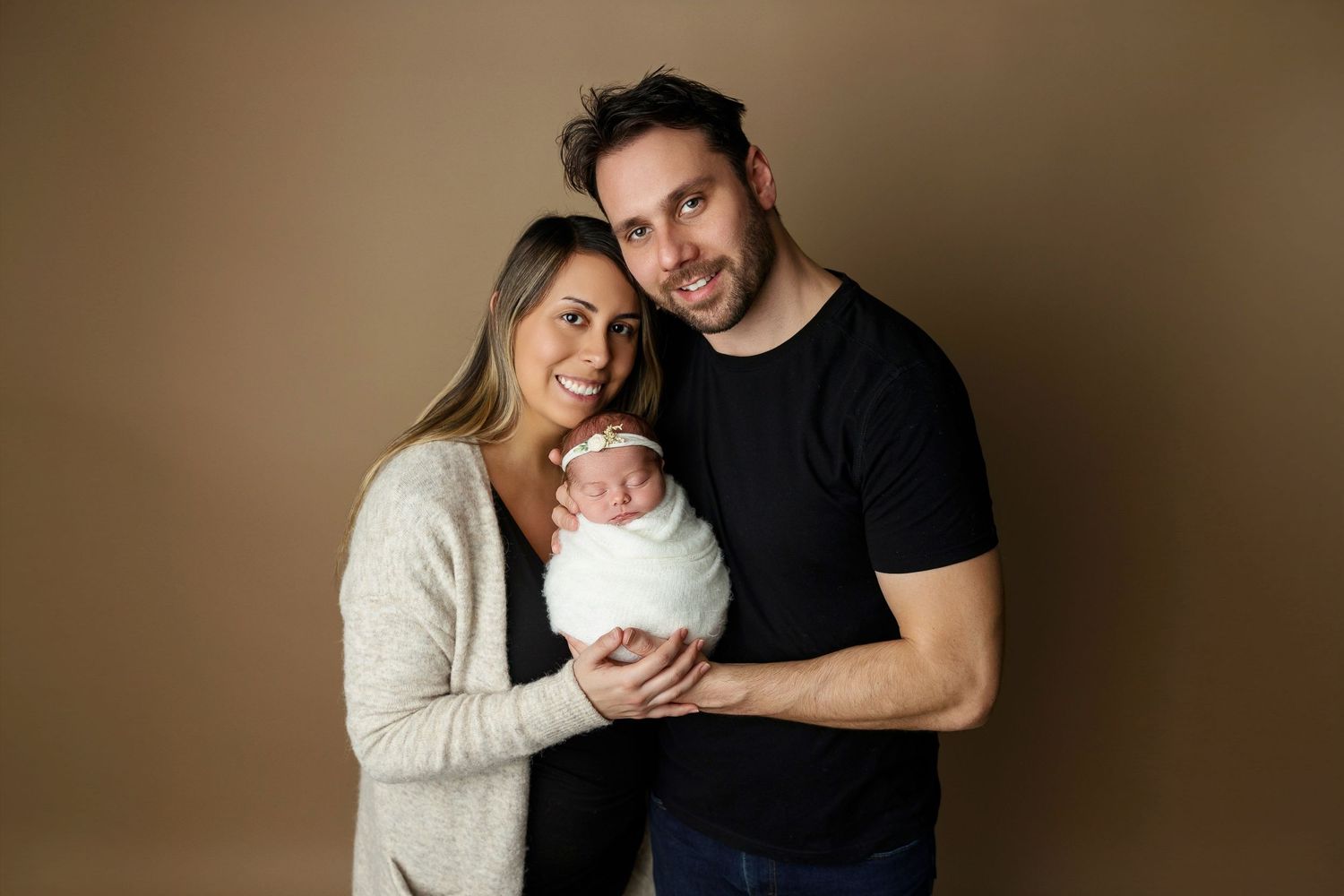 Family of three poses together against brown backdrop in studio setting.