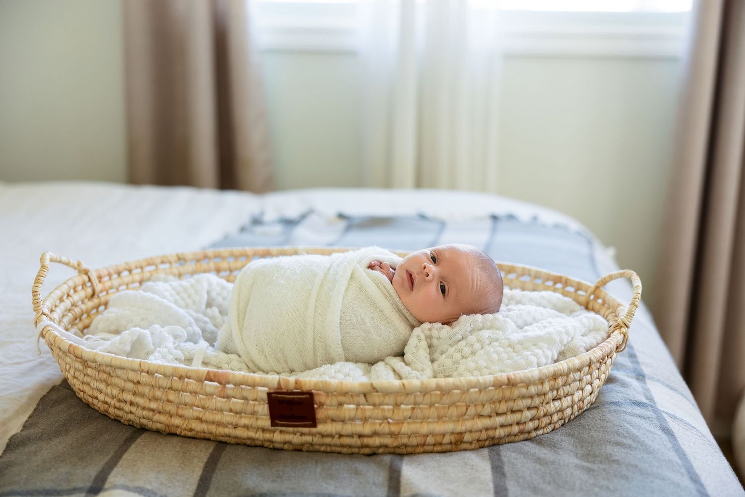 Newborn baby sleeping peacefully in a round woven moses basket on white bedding.
