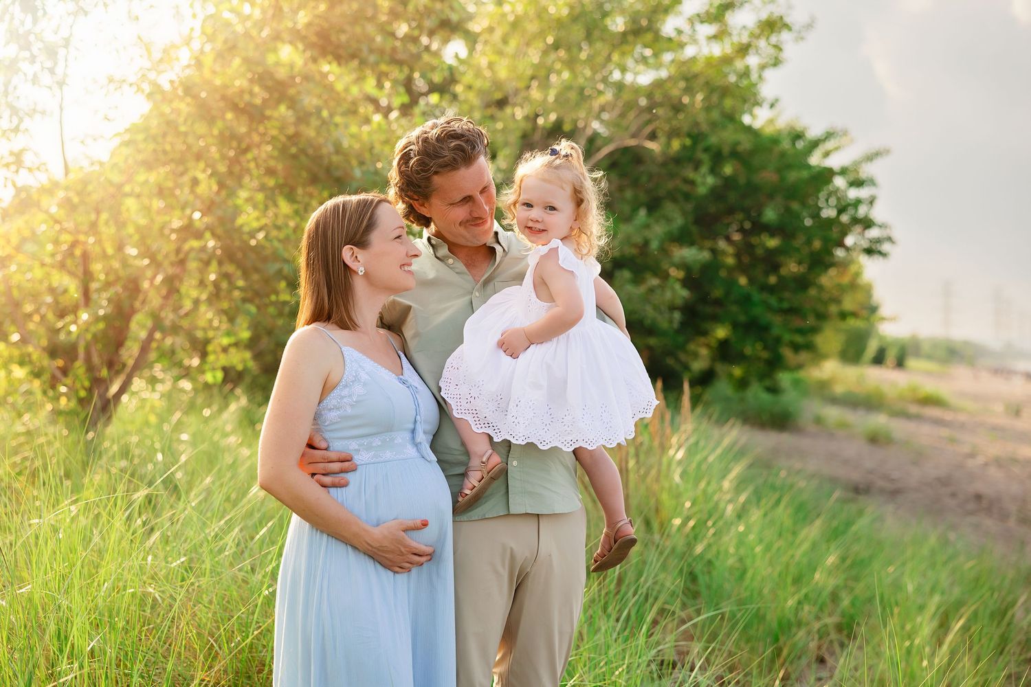 Family shares joyful moment in sunlit field during maternity photoshoot.