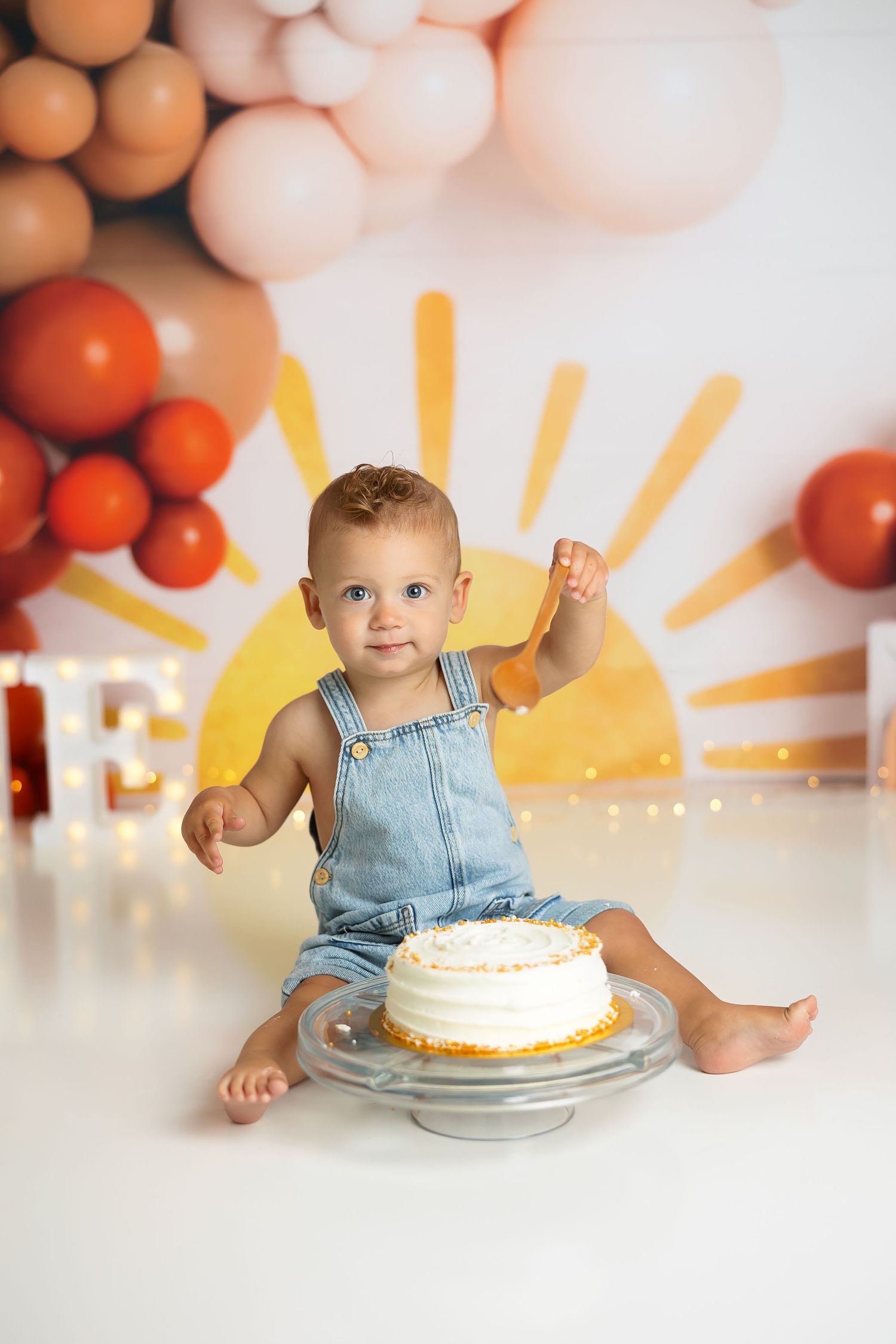 A cake smash session with orange and peach balloons against a yellow sun backdrop.