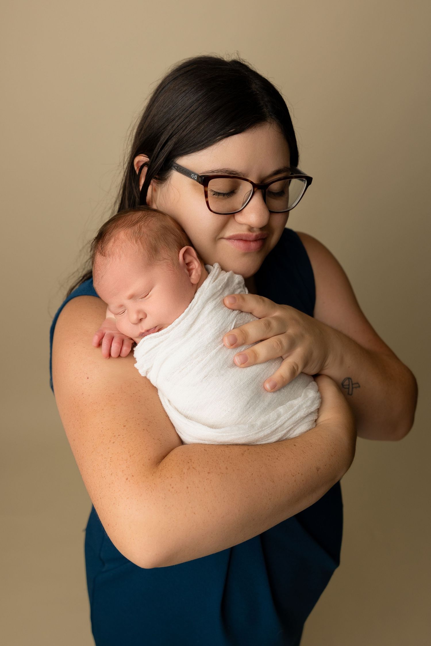 A tender moment of someone in a navy dress holding and gazing at their sleeping newborn baby.