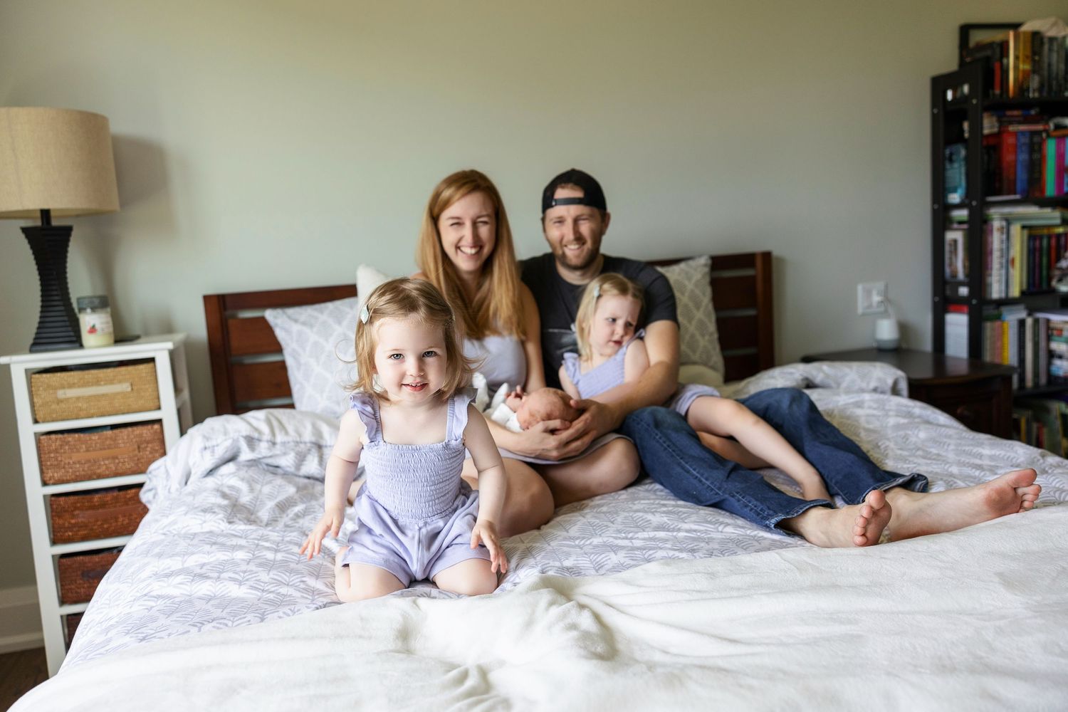 Family with young child enjoy relaxing together on a white comforter bed at home.