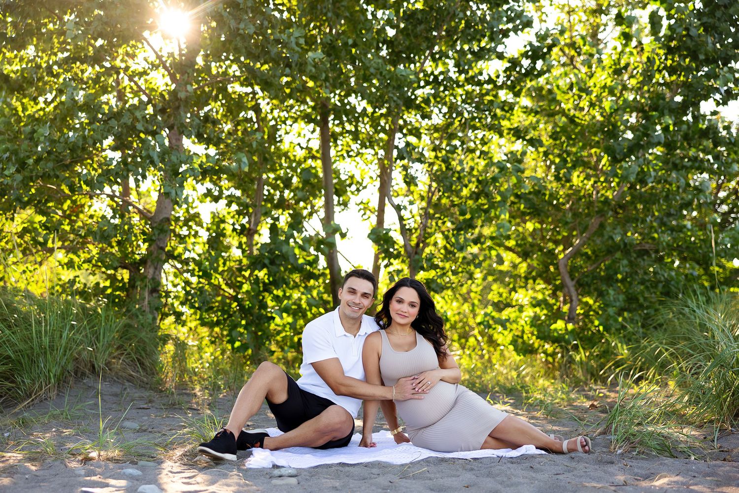 Expectant couple poses together on ground during sunset maternity session.