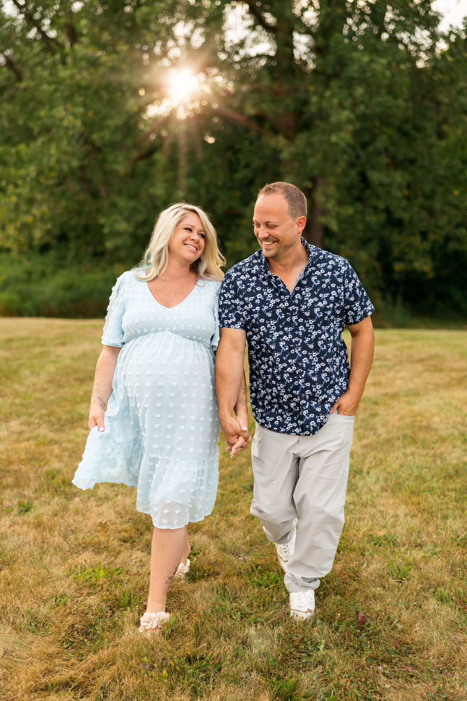 A couple shares a joyful moment walking together on a grassy hillside during golden hour sunset.