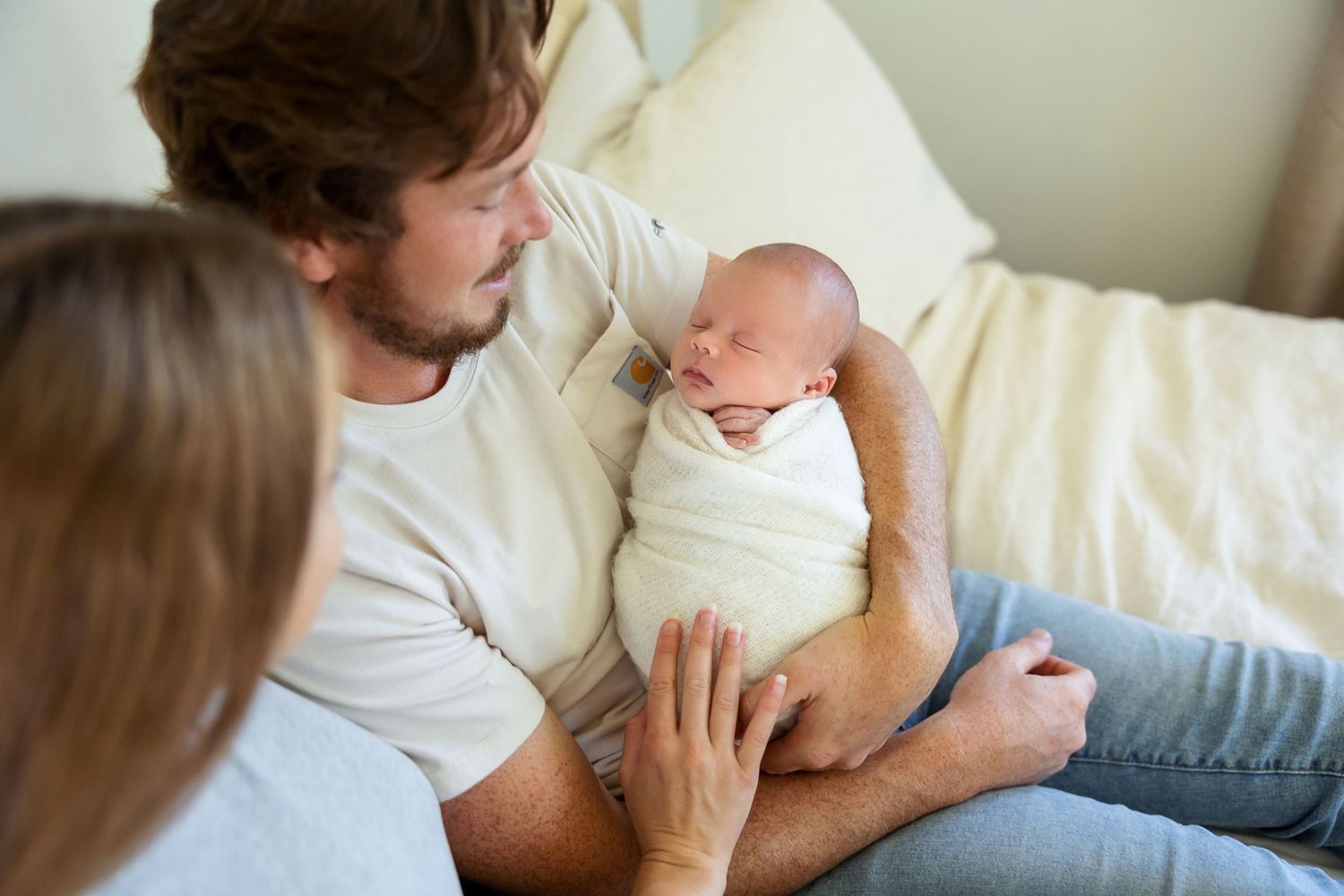 Parent holding and bonding with newborn baby while sitting on couch at home.