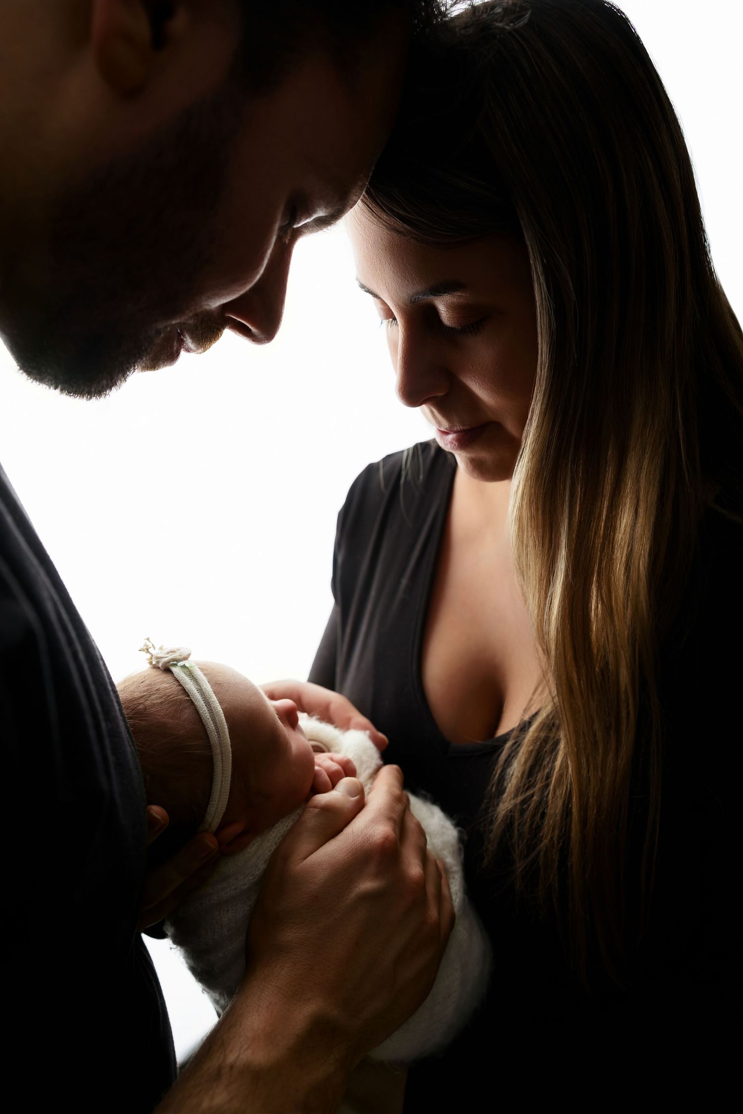 A tender moment captured between parents and their newborn baby in silhouette against a bright background.