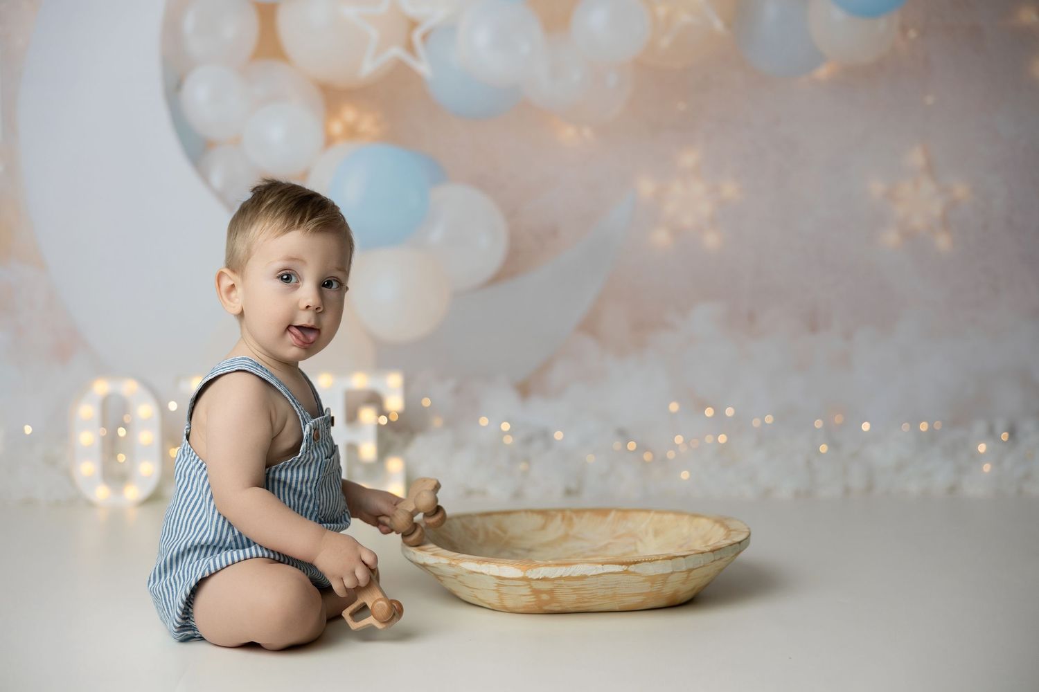 Little one in a diaper scoops frosting from a mixing bowl during a cake smash photo session.