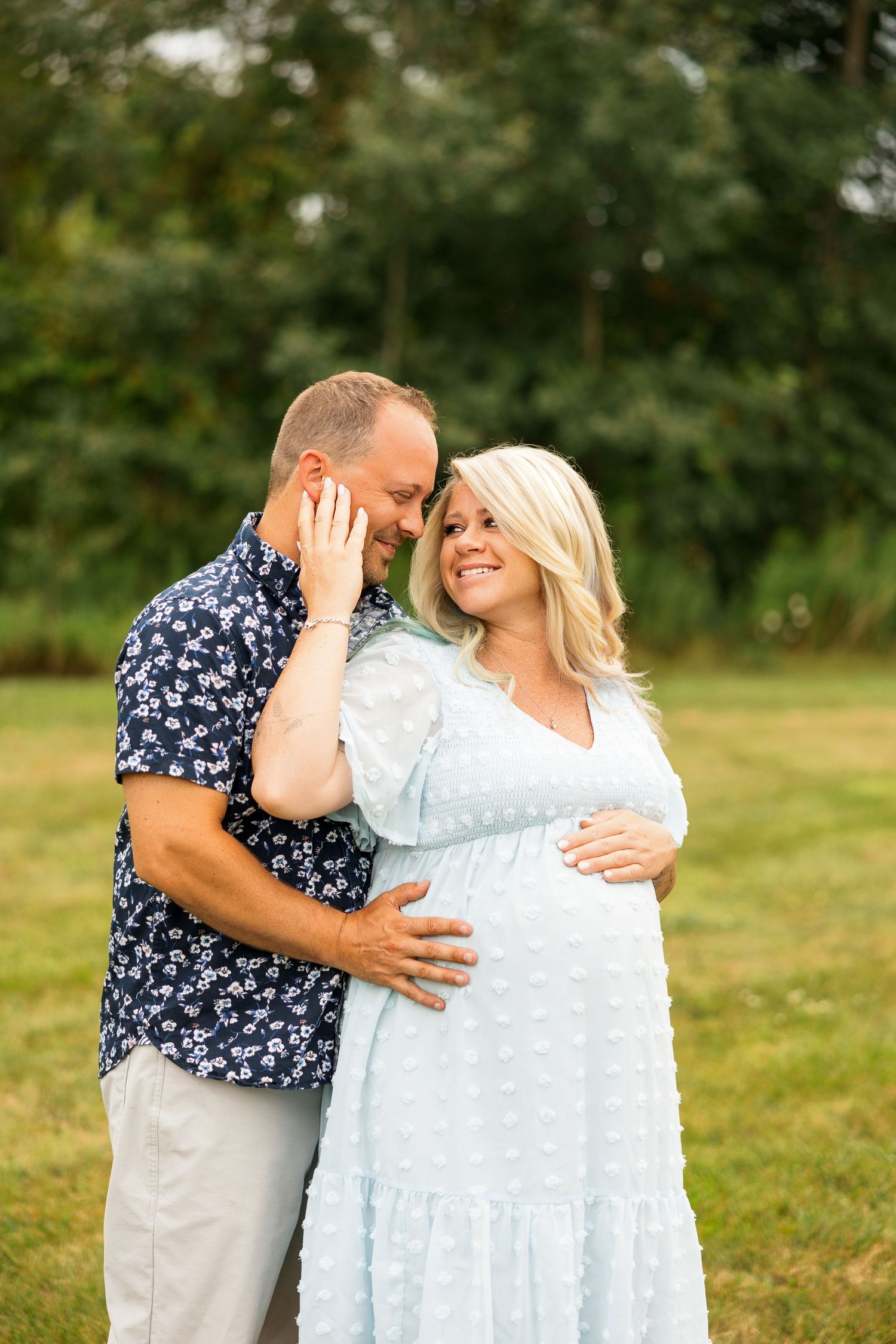 Couple embraces and shares intimate moments in a grassy field during golden hour outdoor photoshoot.