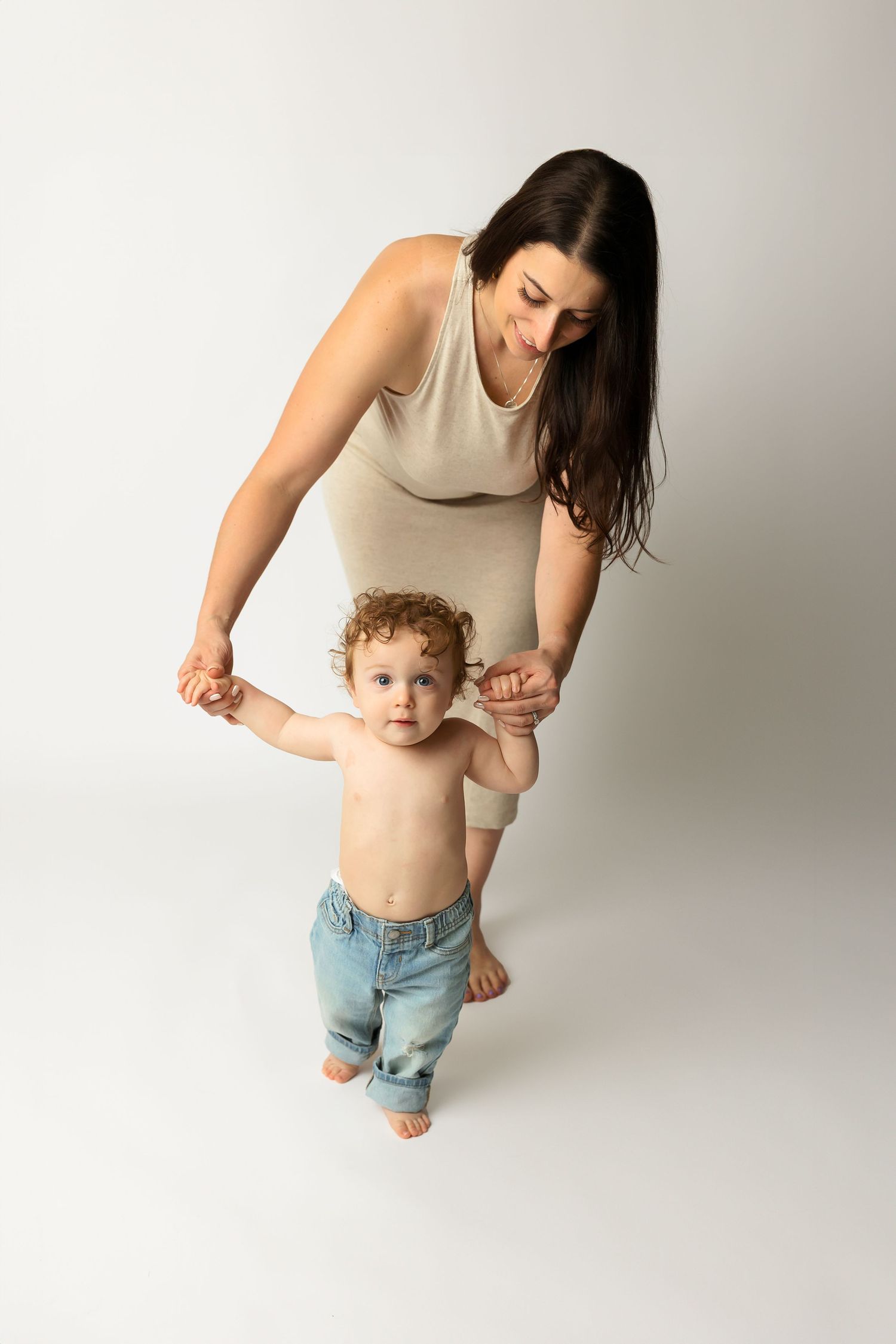 Parent helping toddler take first steps while wearing beige dress and jeans.