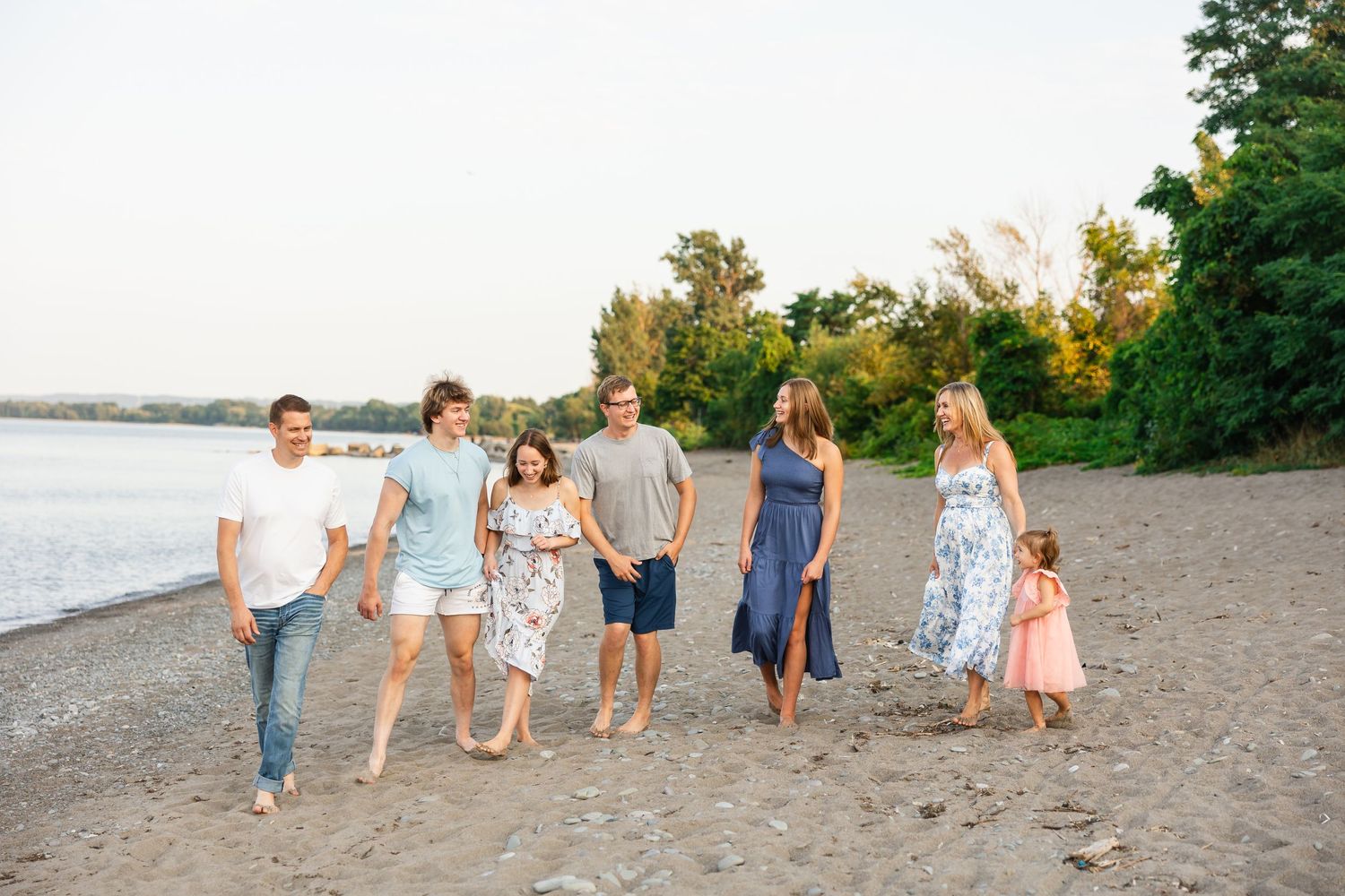 A group of friends walking and laughing together on a sandy beach at sunset along the water's edge.