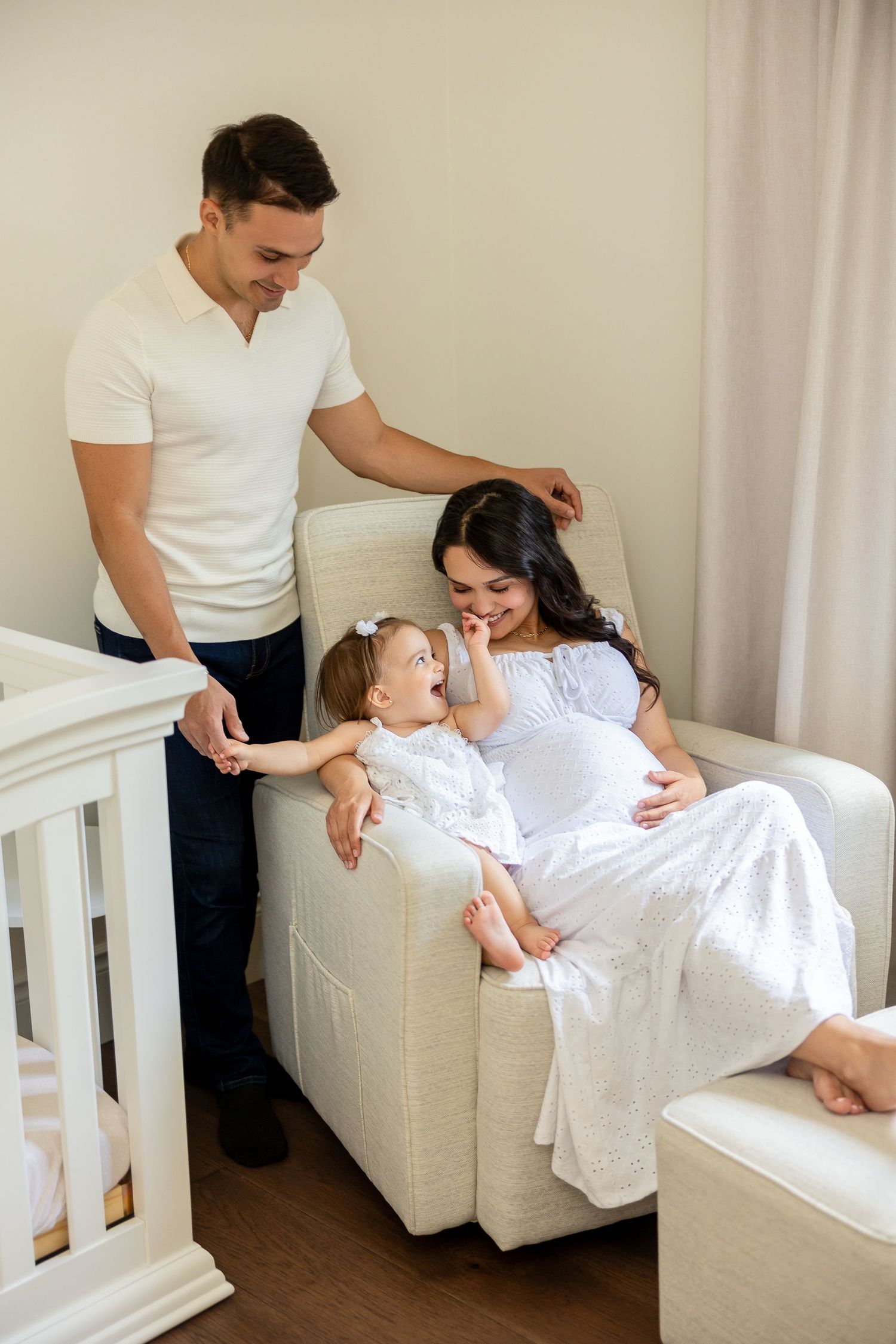 Family session in a bright nursery room featuring white furniture and tender moments with a baby.