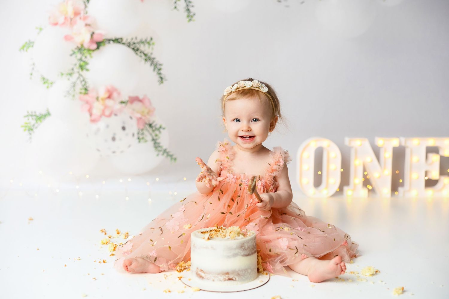 Soft peach and floral themed cake smash setup with delicate flowers and white accents.