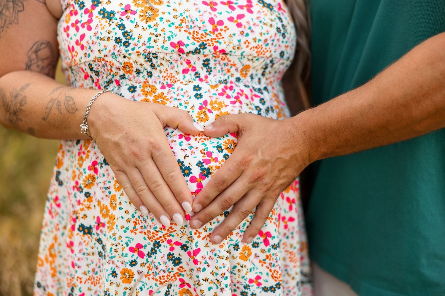 Close-up view of hands resting on a floral print dress showing indications of pregnancy.
