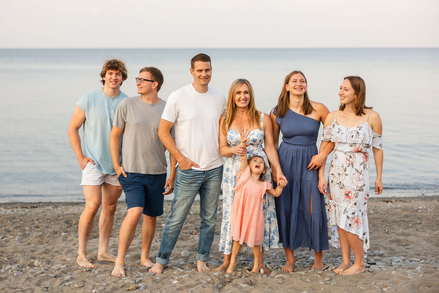 A group enjoying a summer evening together on the beach at sunset, standing by the calm water.
