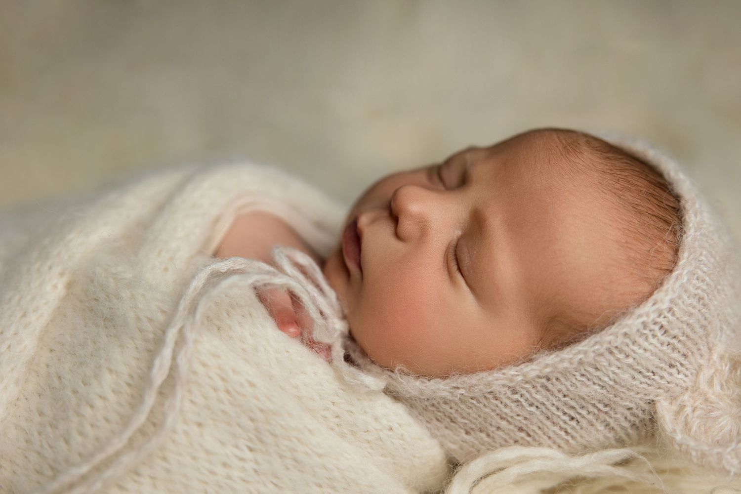 Close-up of sleeping newborn wrapped in soft white knitted blanket.
