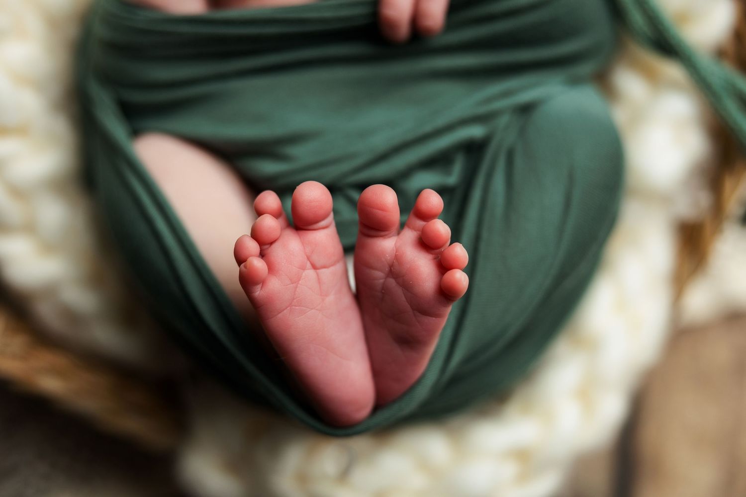 Close-up of tiny baby feet peeking out from green swaddle wrap.