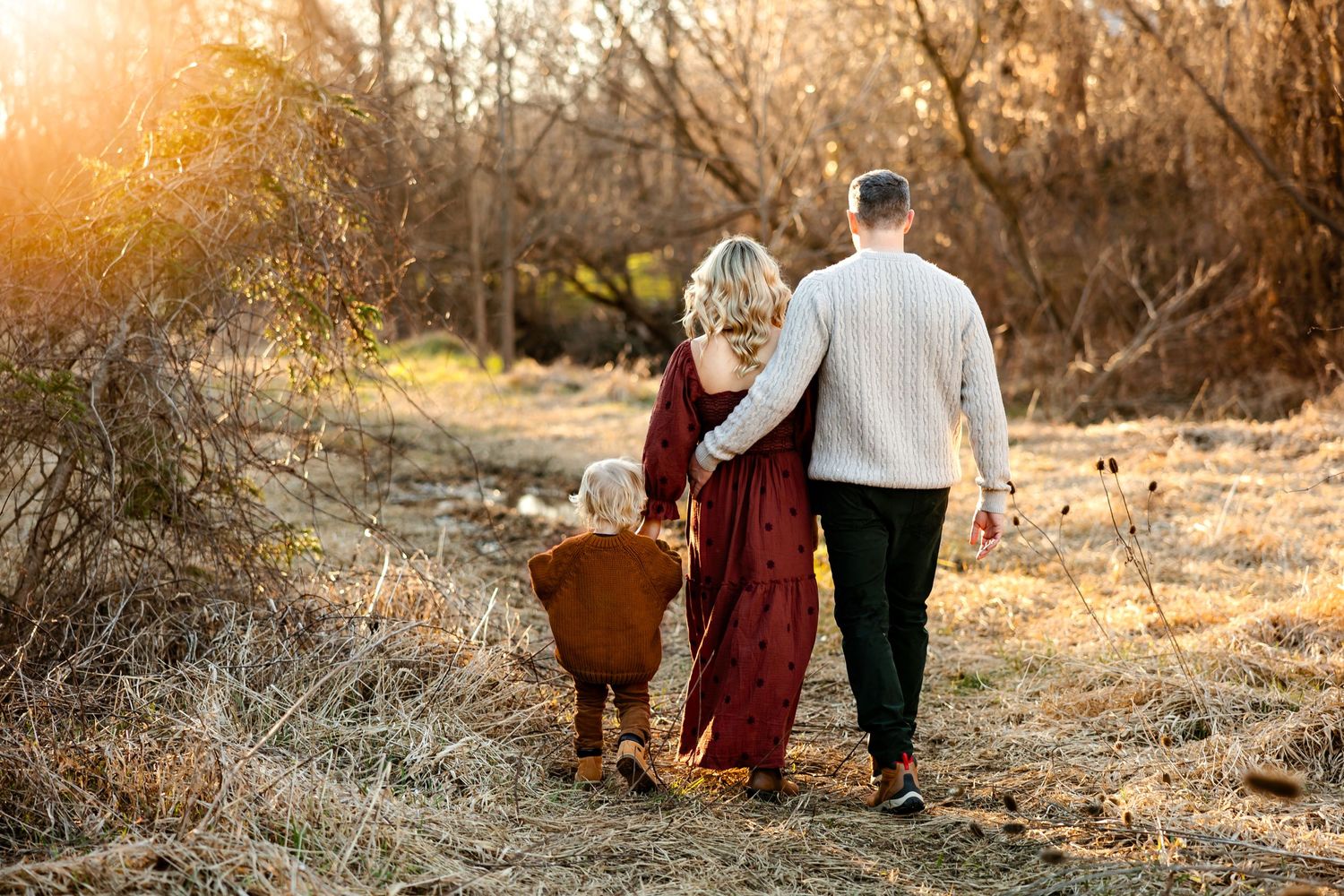 A couple strolls together on a nature trail during golden hour wearing burgundy and cream colored outfits.