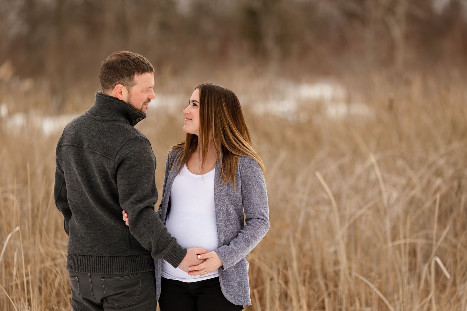 Romantic winter maternity portrait with couple against rustic brown background.