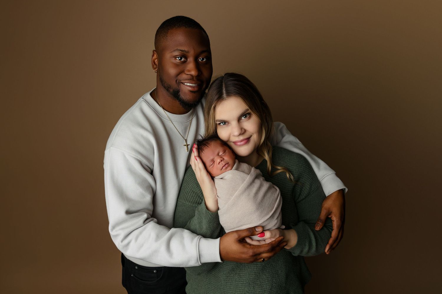 A warm and intimate photoshoot with couples embracing in cozy sweaters against an earthy brown backdrop.